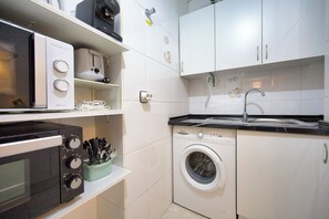Eine kompakte Küche mit Mikrowelle, Backofen, Waschmaschine und Spüle.