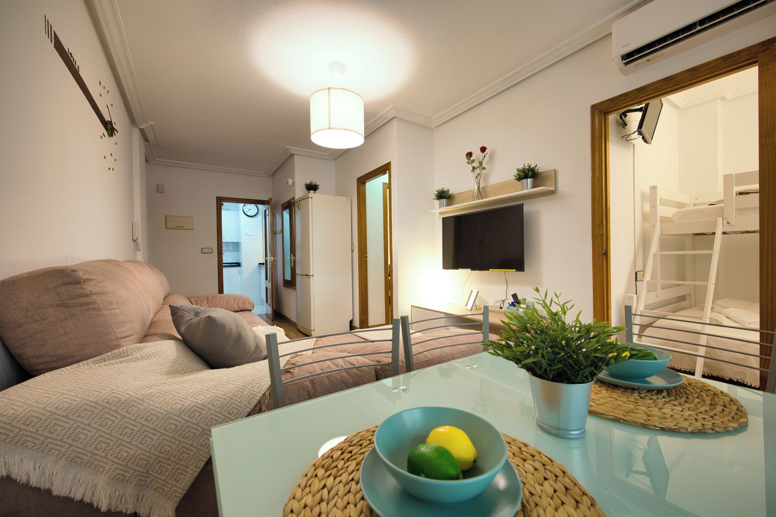 Een moderne woonkamer met een bank, een aan de muur bevestigde televisie en een eethoek met een tafel en stoelen.