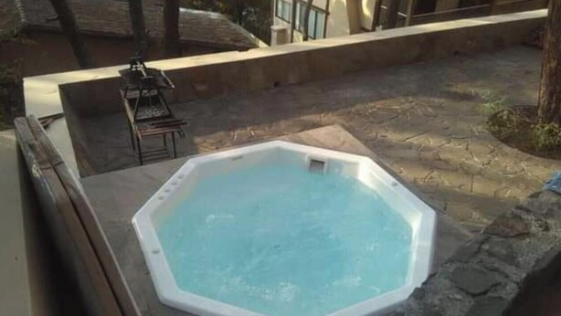 A hot tub in a stone-walled outdoor area with a view of a building in the background. - House in the Woods 9 (Valle de Bravo)