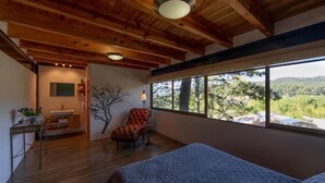 A bedroom with a large window, wooden ceiling beams, a bed, a chair, and a small table with a lamp. - House in the Woods 9 (Valle de Bravo)