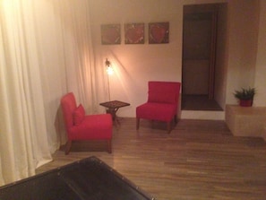 A room with two red chairs, a small table, and a floor lamp. There are three paintings on the wall. - House in the Woods 9 (Valle de Bravo)