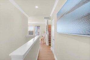 A hallway with a white railing, a staircase, and a large window.