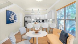 A modern kitchen with white cabinets, a dining area with striped chairs, and a large window with blinds. - Luxury 6BR, Private Pool, Beach Access, Sleeps 20 (Destin)
