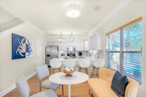 A modern kitchen with white cabinets, a dining area with striped chairs, and a large window with blinds. - Luxury 6BR, Private Pool, Beach Access, Sleeps 20 (Destin)