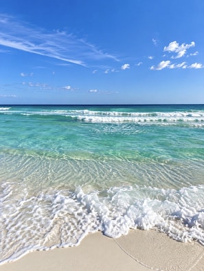 A beach with clear turquoise water, gentle waves, and a clear sky.