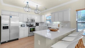 A modern kitchen with white cabinetry, stainless steel appliances, a central island, and pendant lighting. - Luxury 6BR, Private Pool, Beach Access, Sleeps 20 (Destin)