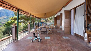 Une terrasse extérieure couverte, avec une table et des chaises, un scooter et une vue sur le paysage environnant.