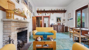 Un salon avec une cheminée, un canapé jaune, une table basse en bois et un coin repas avec une table et des chaises en bois.