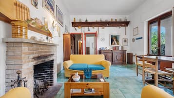 Una sala de estar con chimenea, un sofá amarillo, una mesa de centro de madera y un comedor con mesa y sillas de madera.