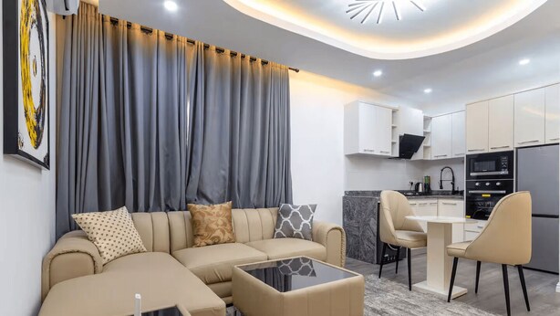 A modern living room with a sofa, coffee table, and chairs, a kitchen with cabinets and appliances, and a dining area with a table and chairs. - Cozy 1-Bedroom Apartment in Lekki 1 with Fast Wi-Fi & 24/7 Power (Lagos)