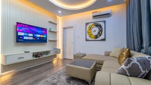 A modern living room with a flat-screen TV, a sofa, a coffee table, and a decorative wall piece. - Cozy 1-Bedroom Apartment in Lekki 1 with Fast Wi-Fi & 24/7 Power (Lagos)