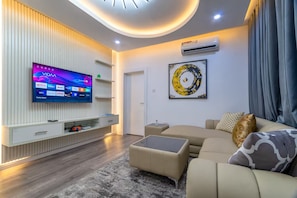 Ein modernes Wohnzimmer mit Flachbildfernseher, einer Couch, einem Couchtisch und einer Wanddekoration.