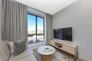 A hotel room with a sofa, a coffee table, a TV, and a large window with curtains. - One Rosebank: Where Style Meets Convenience (Johannesburg)