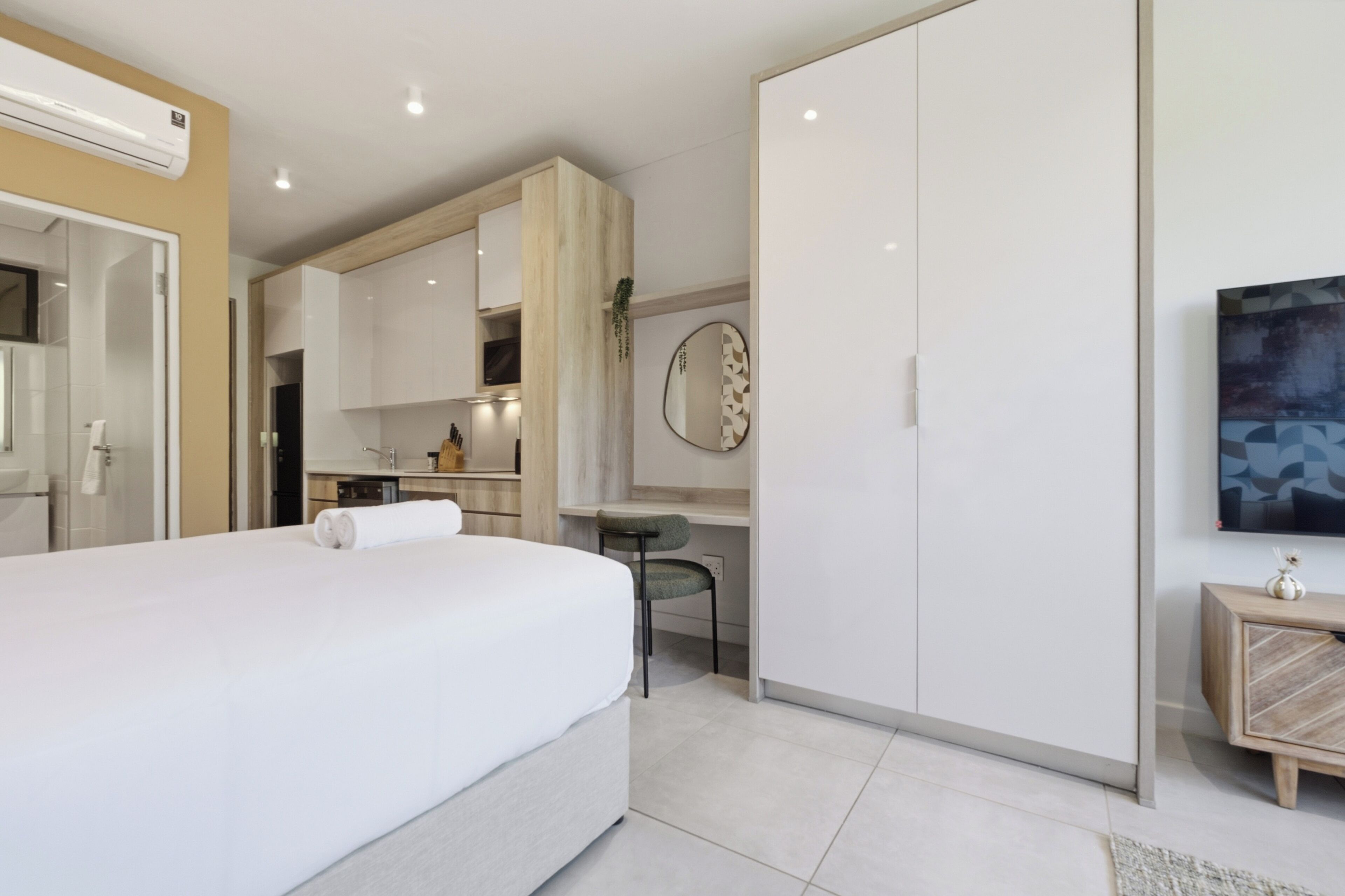 A modern hotel room with a large bed, a desk, and a wardrobe.