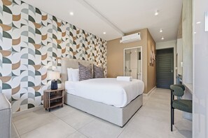A modern bedroom with a geometric-patterned wall, a large bed, a bedside table, and a chair. - Zimbali Lakes Studio | Rooftop Pool, Balcony (Westbrook)