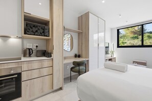 Ein modernes Schlafzimmer mit einem großen Bett, einem Schreibtisch mit Stuhl, einem Kleiderschrank und einem Fenster mit Blick ins Grüne.