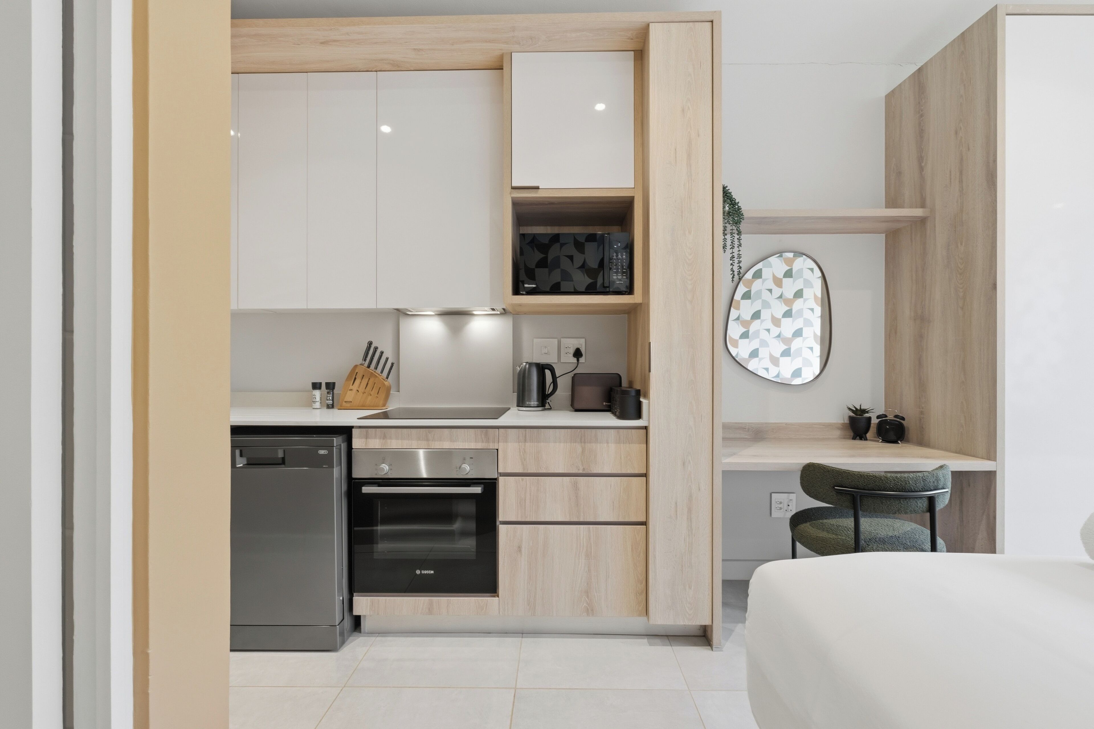 A modern kitchen with a dishwasher, oven, and microwave. There is a small dining area with a chair and a table.