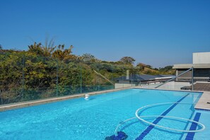 Ein klarer, blauer Swimmingpool mit Glasbarriere, umgeben von üppiger Bepflanzung und einem modernen Gebäudebau.