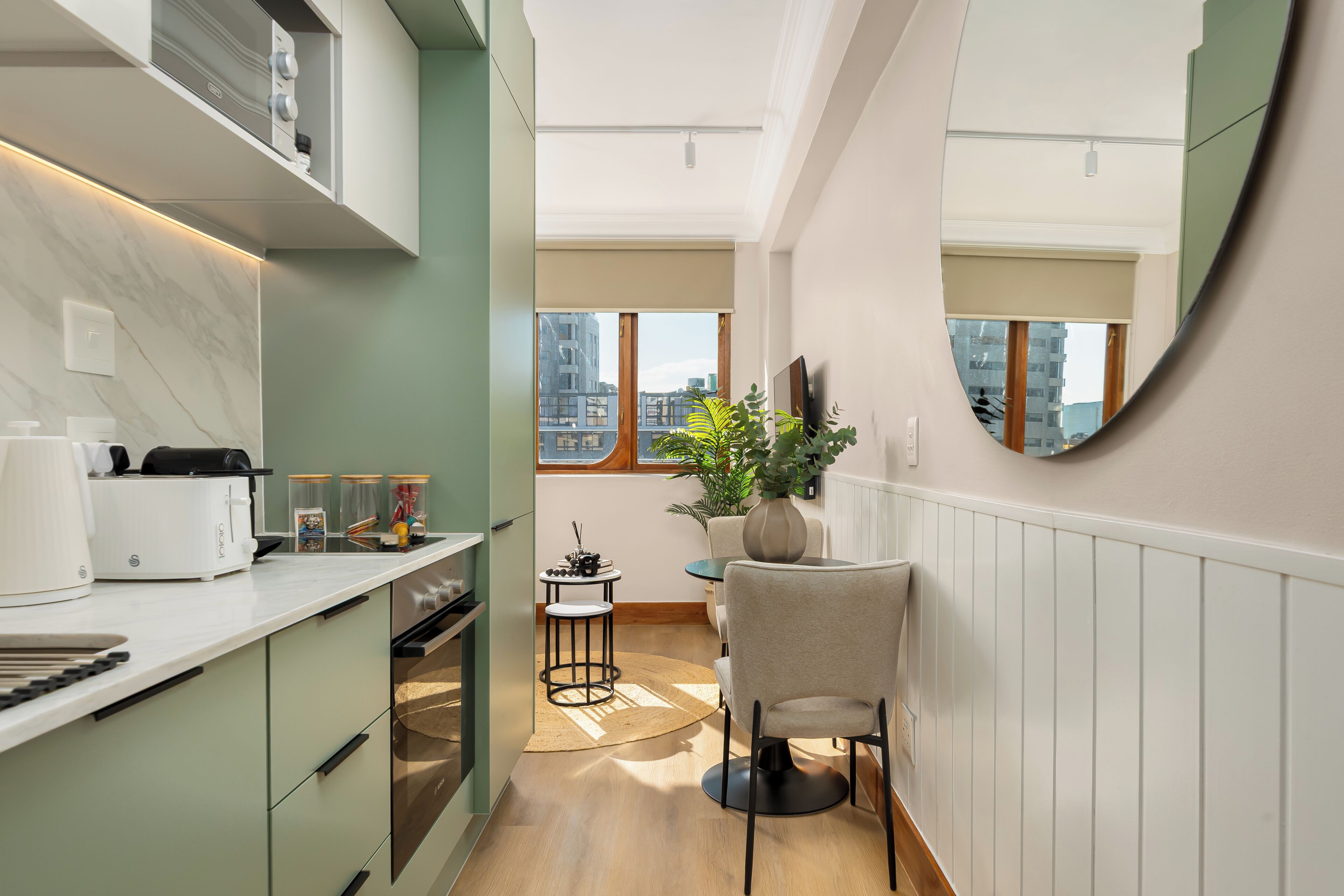 A modern kitchen with a dining area, a large mirror, and a view of the cityscape.