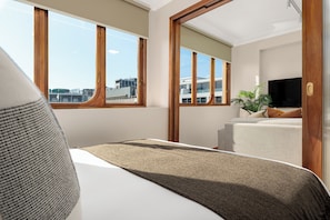 A hotel room with a large window, a bed, a television, and a plant. - Charlie and the Chairman | Cape Town City Base (Cape Town)