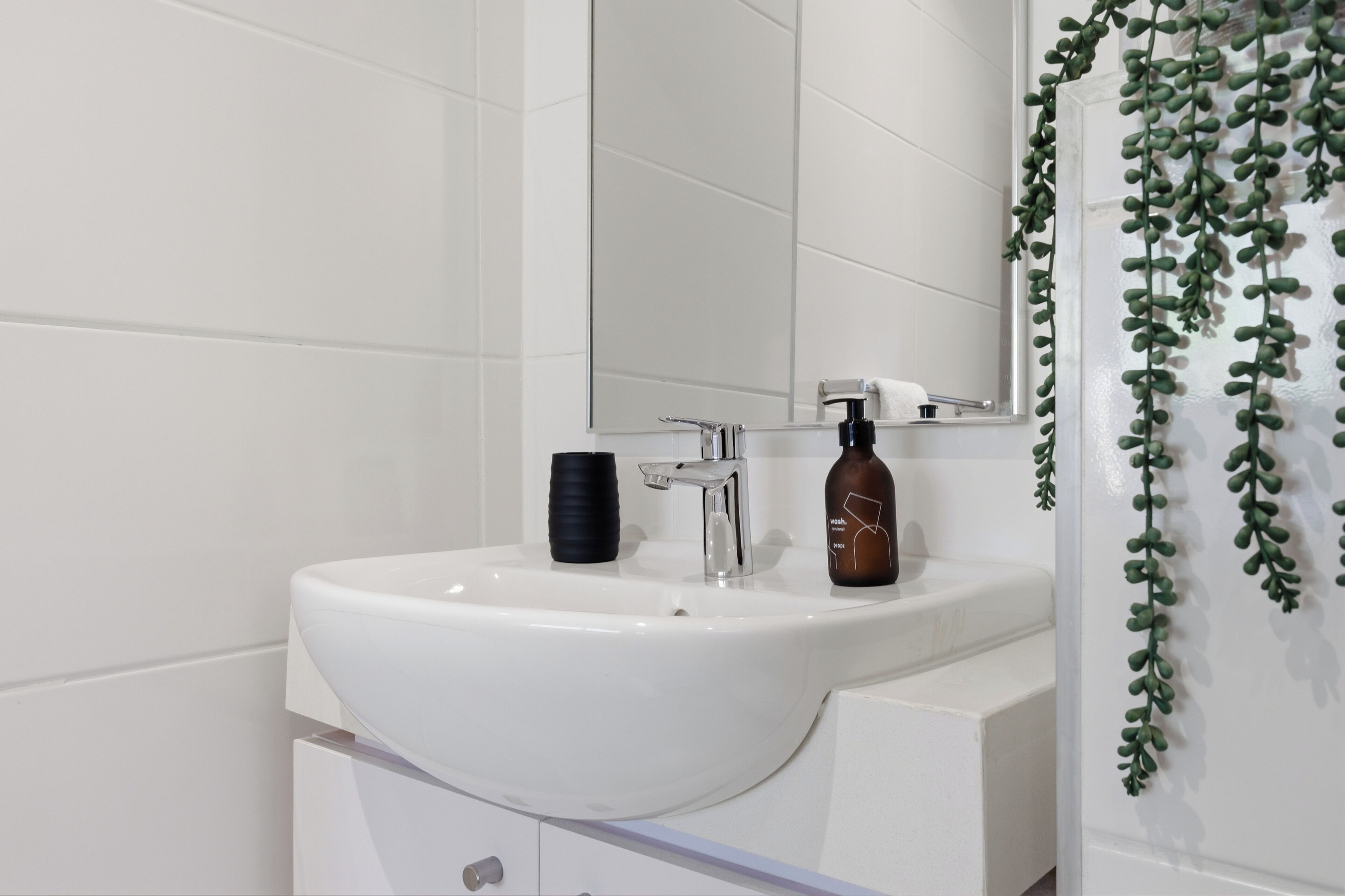 A white bathroom sink with a mirror above it, a soap dispenser, and a towel rack.