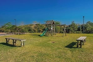 Ein Spielplatz mit Rutsche und Klettergerüsten, umgeben von Gras und Bäumen.