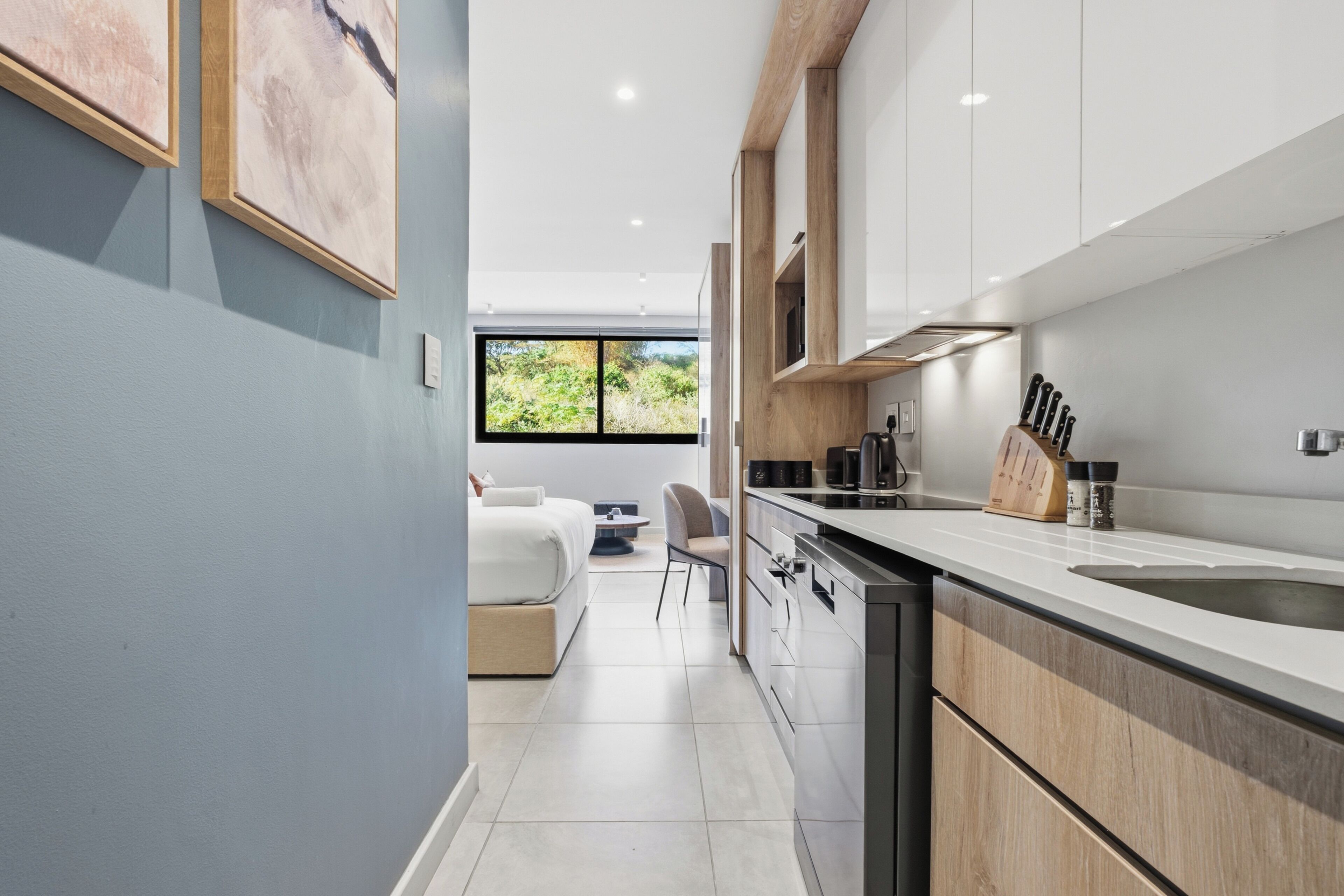 A modern kitchen with a large window, white cabinetry, and a dining area with a sofa and table.