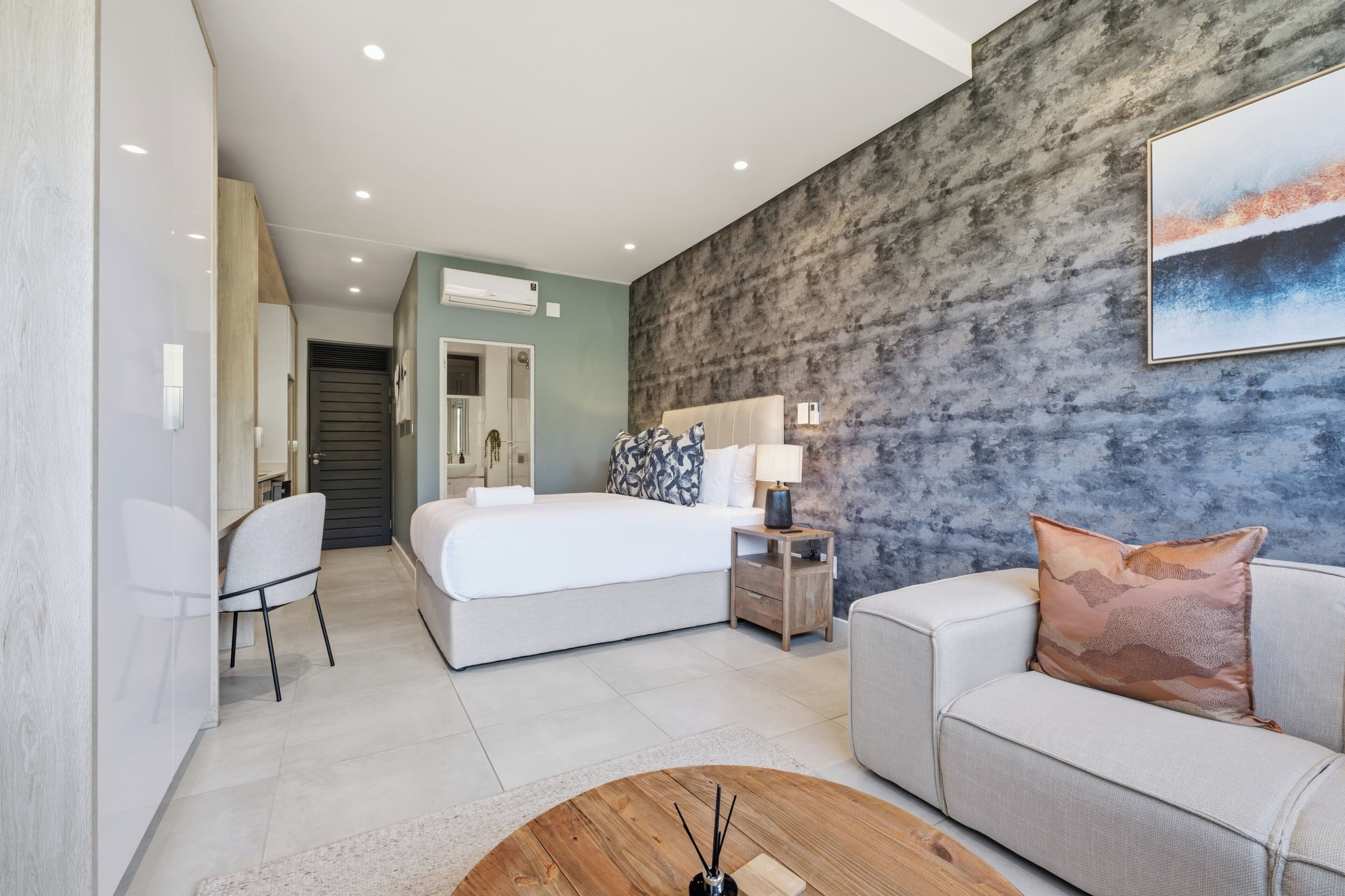 Une chambre d’hôtel moderne avec un lit, un canapé, une table basse et un tableau au mur.