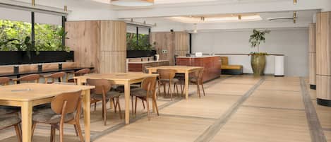 A modern dining area with wooden tables and chairs, a large pendant light, and a view of greenery outside.