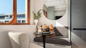 Ein modernes Zimmer mit einem runden Spiegel, einem kleinen Tisch mit Büchern und einer Pflanze, einem Sofa und Blick auf ein Gebäude.