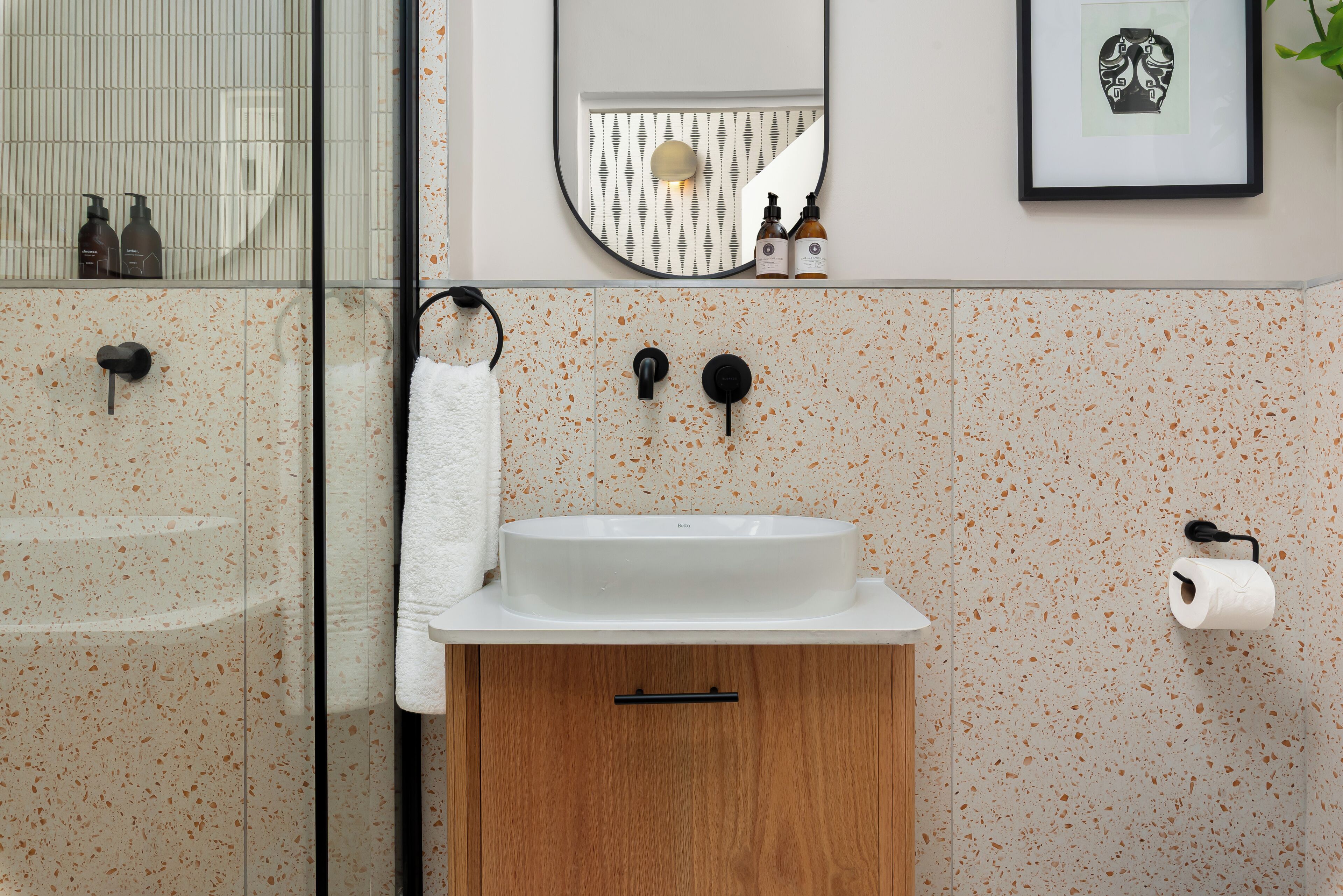 Et badeværelse med en hvid vask, et spejl og en toiletpapirholder.