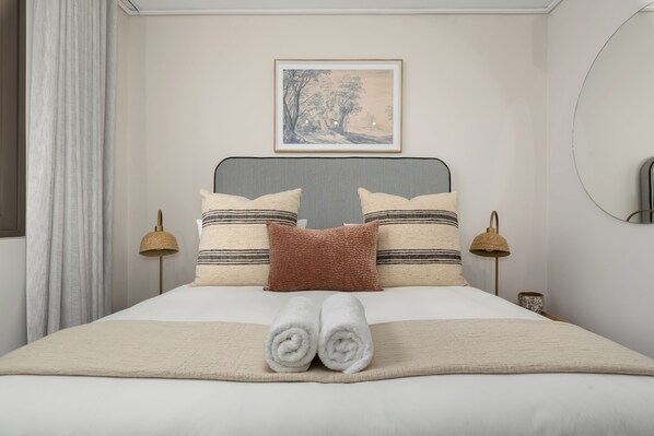 Uma cama bem arrumada com cabeceira listrada, duas luminárias de cabeceira e um quadro emoldurado acima da cama.