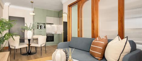 A modern living room with a grey sofa, a small round coffee table, and a dining area with a white table and chairs.