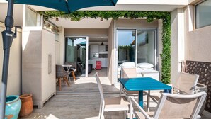 A patio area with a table and chairs, a sliding glass door leading to a kitchen, and a green plant wall. - Le Jardin de La Plage - Climatisé et plage à 100 m (Canet-en-Roussillon)
