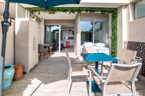 Eine Terrasse mit Tisch und Stühlen, eine Glasschiebetür, die zu einer Küche führt, und eine grüne Wand aus Pflanzen.