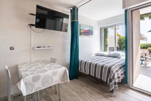 Ein Zimmer mit einem Bett, einem Tisch, einem an der Wand befestigten Fernseher und einem Fenster mit Vorhängen.