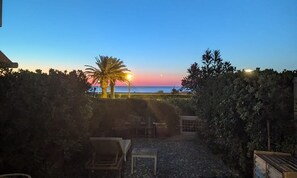 A patio area with a view of the sea at sunset, a palm tree, and outdoor furniture. - Le Jardin de La Plage - Climatisé et plage à 100 m (Canet-en-Roussillon)