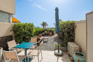 Eine Terrassenfläche mit Gartenmöbeln, einem Tisch und einem blauen Sonnenschirm.