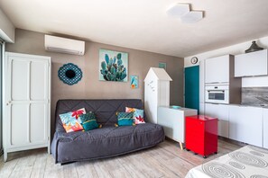 Ein kompakter Wohnbereich mit Sofa, einer kleinen Küchenzeile und einem dekorativen Kakteenbild.