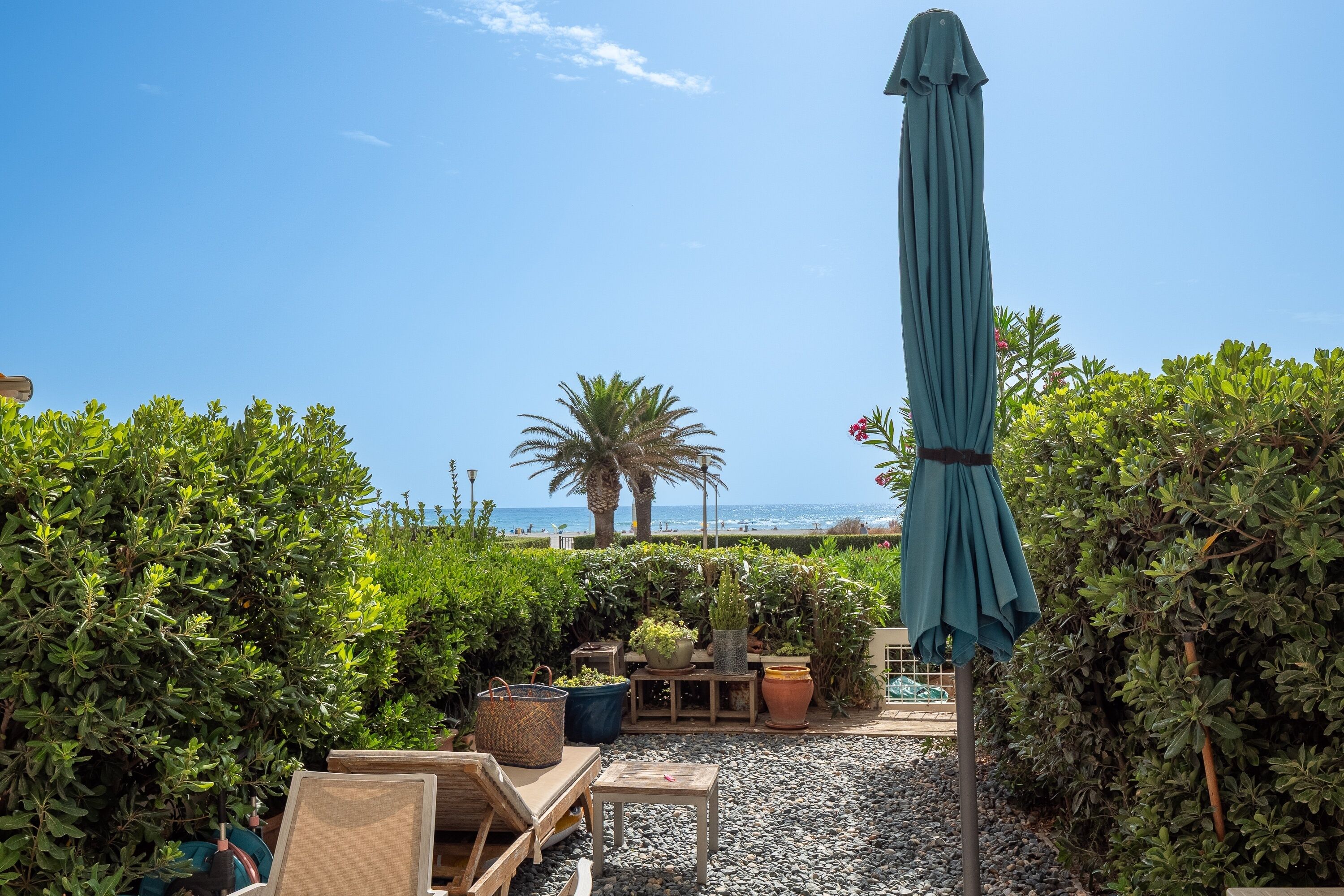 A patio area with a view of the beach, outdoor furniture, and a large umbrella.