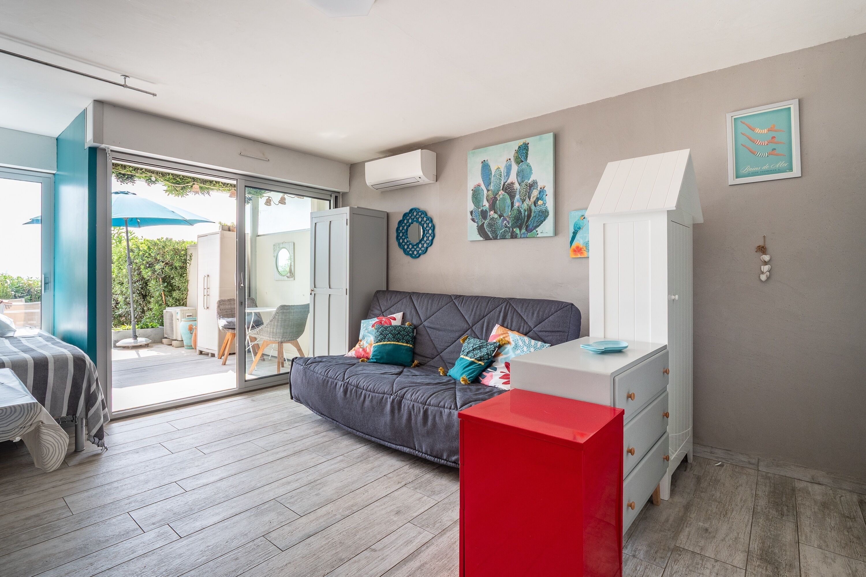 A modern bedroom with a grey sofa, a red cabinet, and a glass door leading to a balcony.