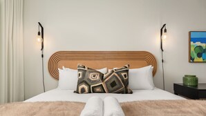 Ein Bett mit Holz-Kopfteil, zwei Nachttischlampen, ein Bild an der Wand und eine grüne Vase auf einem Nachttisch.