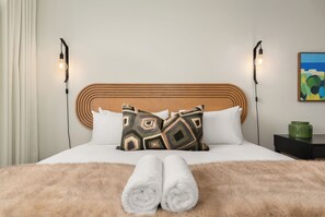 Ein Bett mit Holz-Kopfteil, zwei Nachttischlampen, ein Bild an der Wand und eine grüne Vase auf einem Nachttisch.