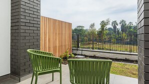 Ein Balkon mit zwei grünen Stühlen, einem Holzzaun und Blick auf einen Garten mit Palmen.