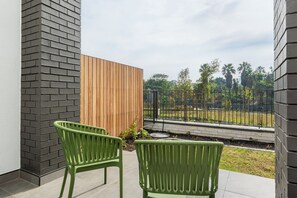 Ein Balkon mit zwei grünen Stühlen, einem Holzzaun und Blick auf einen Garten mit Palmen.