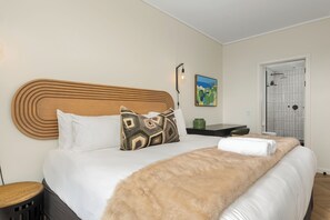 Een hotelkamer met een groot bed, een houten hoofdeinde, een schilderij aan de muur en een deur naar de badkamer.