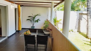 A covered outdoor area with a table and chairs, a potted plant, and a view of a garden. - La Case Coco - Bananes - Appartement climatisé (Saint Joseph)