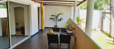 Un espacio exterior cubierto con una mesa y sillas, una planta en maceta y vistas a un jardín.