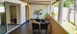 A covered outdoor area with a table and chairs, a potted plant, and a view of a garden. - La Case Coco - Bananes - Appartement climatisé (Saint Joseph)