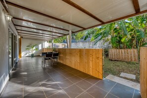 A covered outdoor area with a tiled floor, wooden furniture, and a view of tropical vegetation. - La Case Coco - Bananes - Appartement climatisé (Saint Joseph)